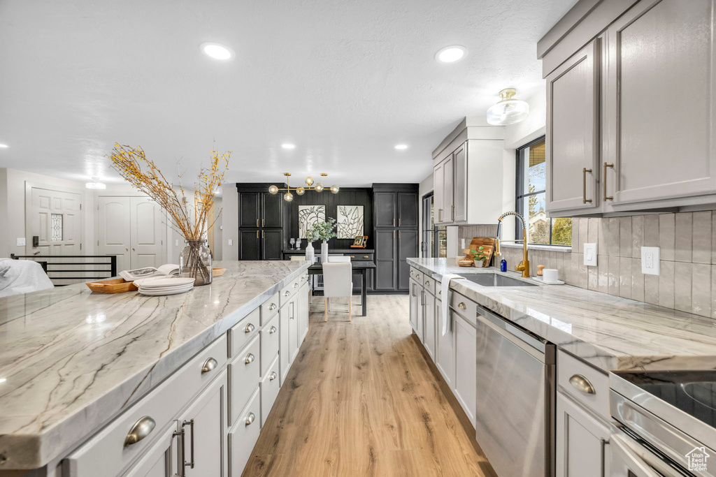 Kitchen with light stone counters, tasteful backsplash, light hardwood / wood-style floors, sink, and dishwasher
