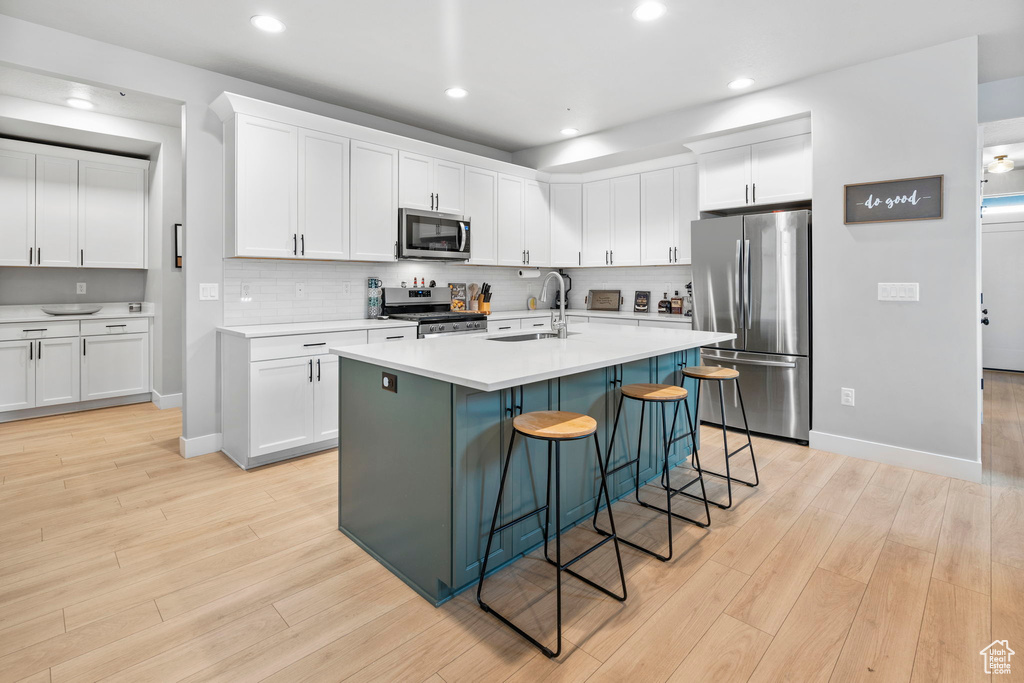 Kitchen featuring light hardwood / wood-style flooring, a kitchen breakfast bar, white cabinetry, an island with sink, and appliances with stainless steel finishes