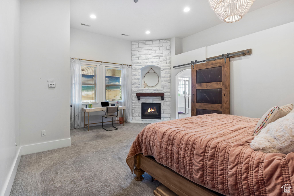 Bedroom with a fireplace, a barn door, and light colored carpet