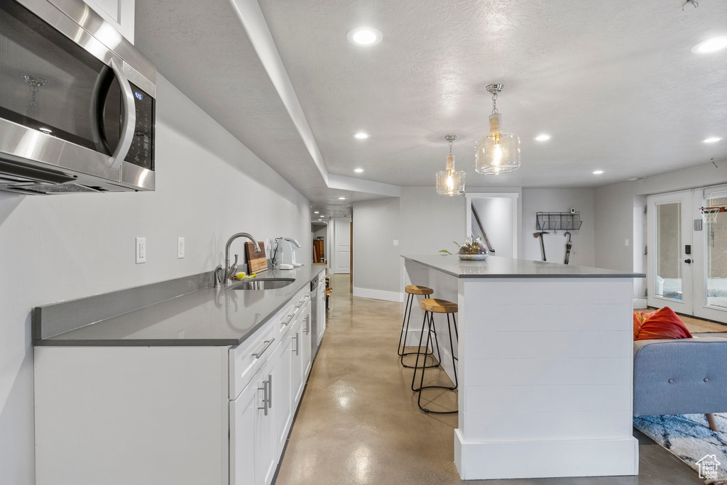 Kitchen featuring white cabinetry, hanging light fixtures, appliances with stainless steel finishes, a kitchen breakfast bar, and sink