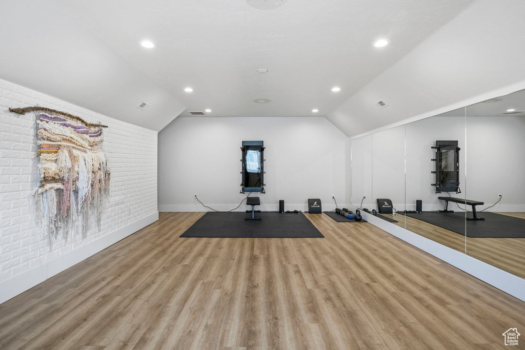 Exercise area featuring brick wall, light hardwood / wood-style flooring, and lofted ceiling