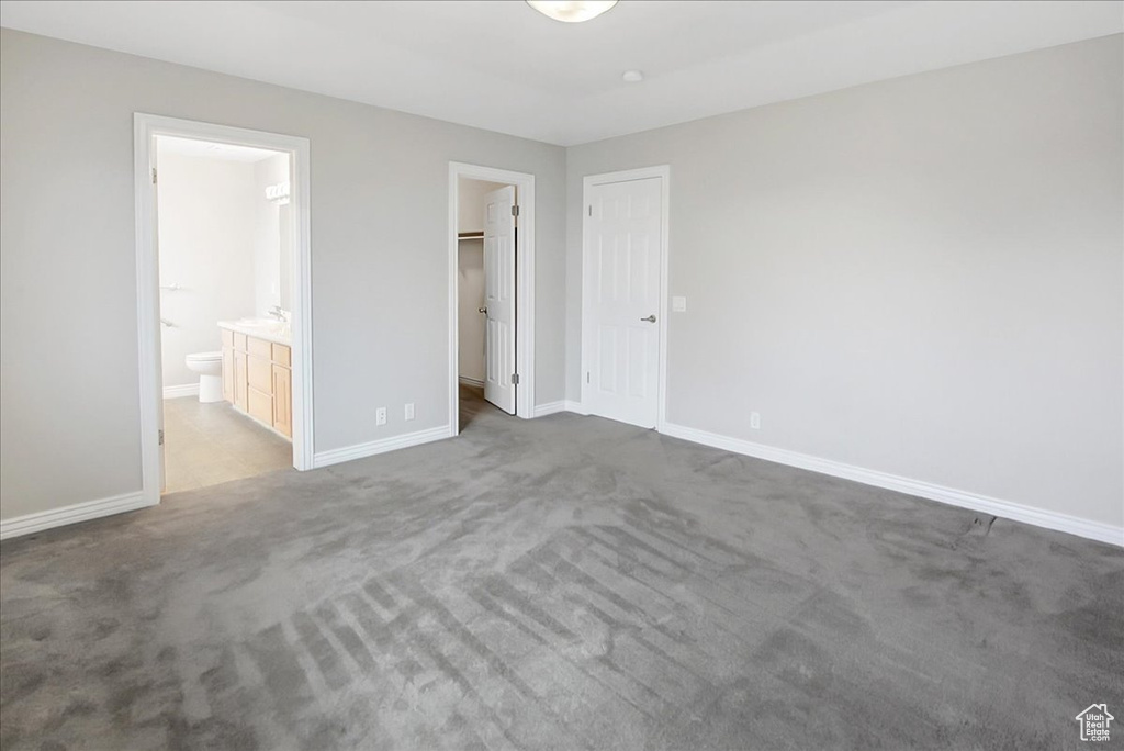 Unfurnished bedroom featuring a spacious closet, light colored carpet, ensuite bathroom, and a closet