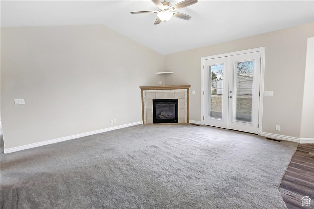 Unfurnished living room with french doors, carpet flooring, vaulted ceiling, ceiling fan, and a tile fireplace