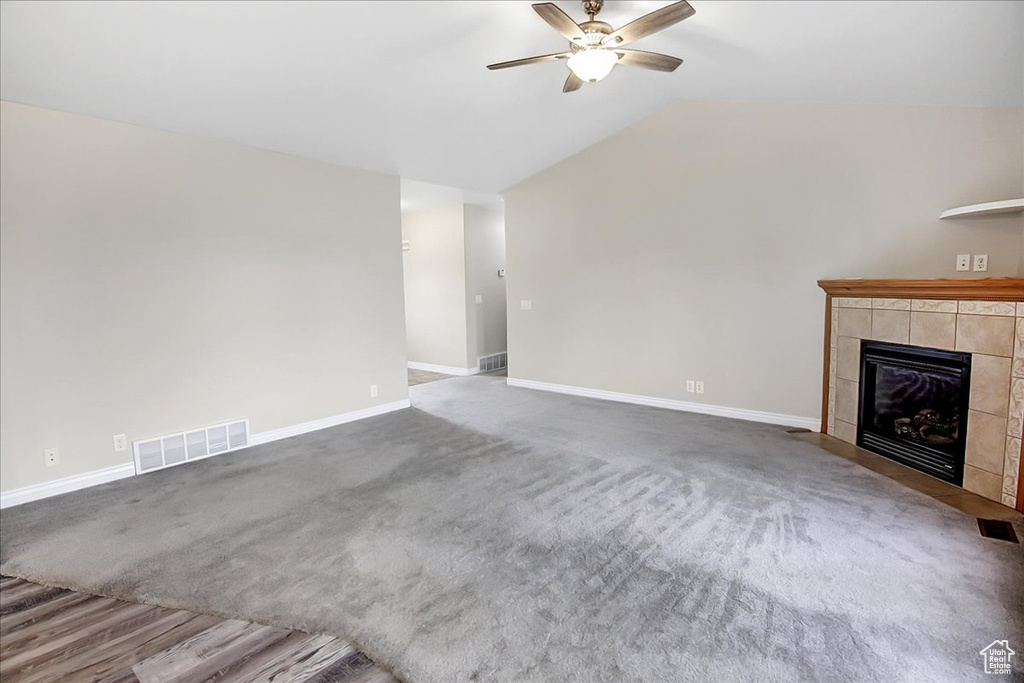 Unfurnished living room featuring dark carpet, vaulted ceiling, ceiling fan, and a tile fireplace