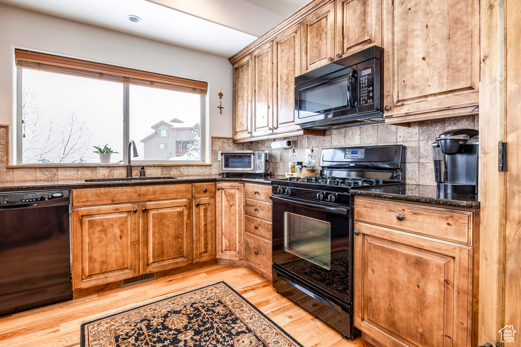 Kitchen featuring tasteful backsplash, sink, black appliances, and light wood-type flooring