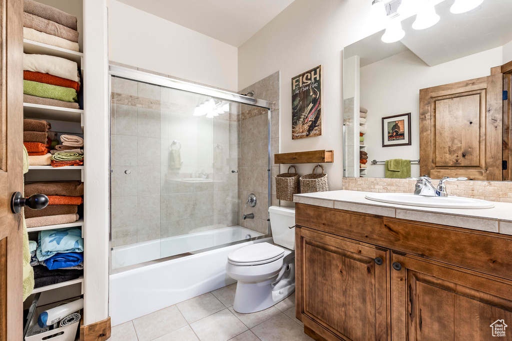 Full bathroom with combined bath / shower with glass door, vanity, tile floors, and toilet
