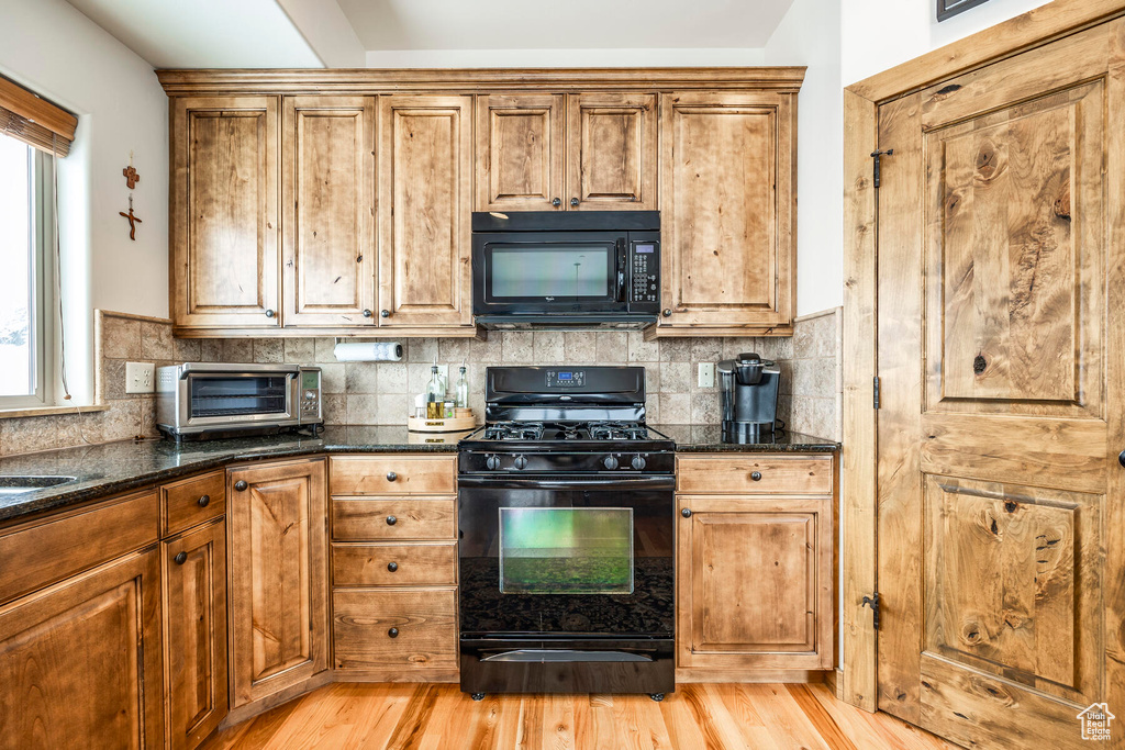 Kitchen with dark stone counters, backsplash, black appliances, and light wood-type flooring