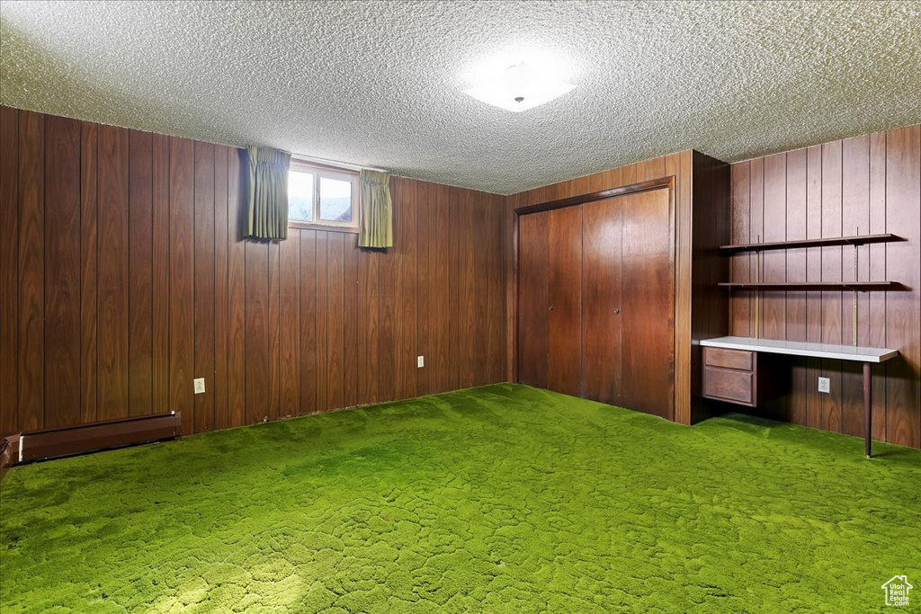 Basement with wooden walls, baseboard heating, a textured ceiling, and carpet