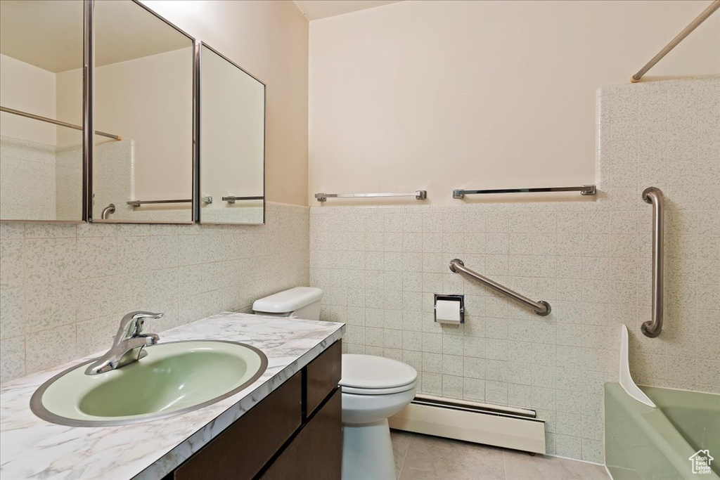 Full bathroom with large vanity, a baseboard radiator, tiled shower / bath, toilet, and tile floors
