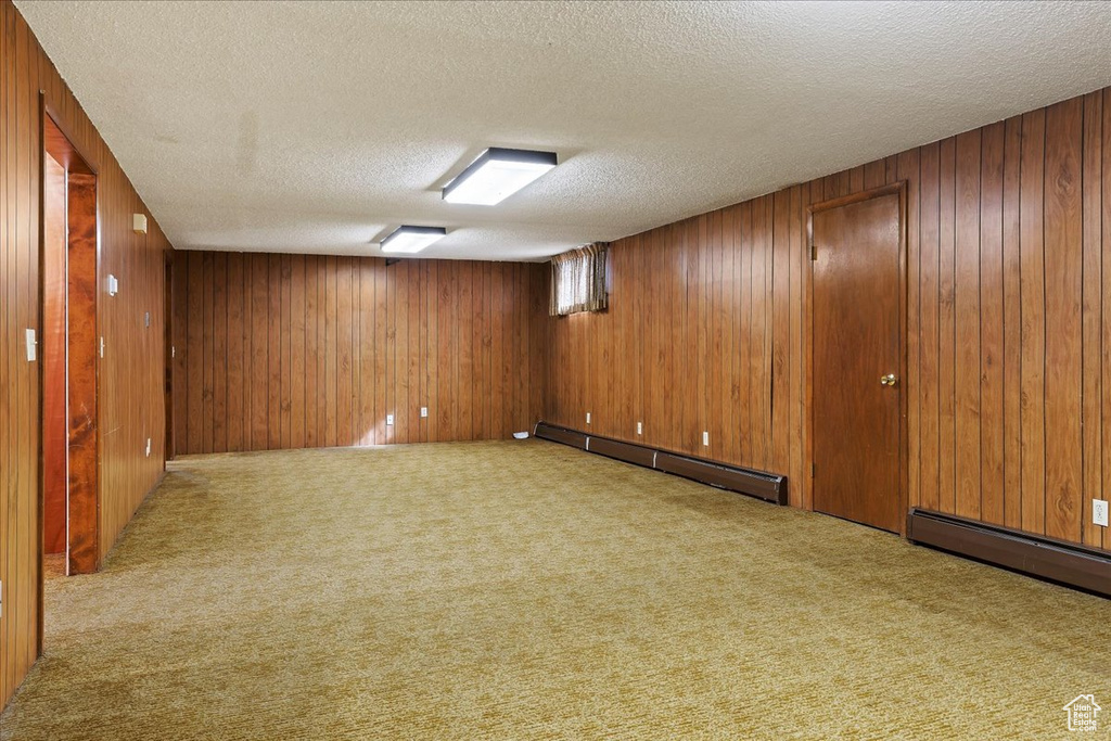Basement featuring a baseboard radiator, wooden walls, a textured ceiling, and carpet flooring