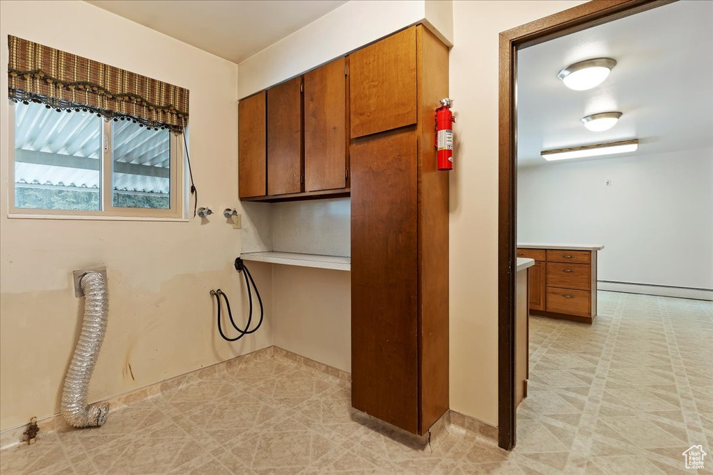Clothes washing area featuring a baseboard radiator, light tile floors, electric dryer hookup, and cabinets