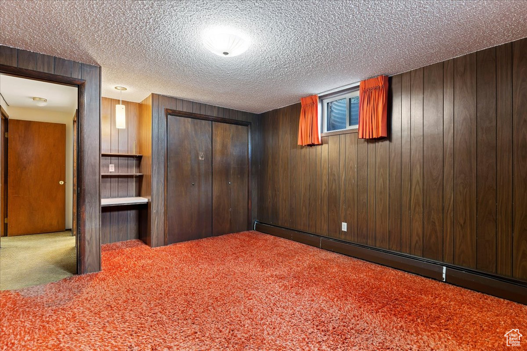Basement with a baseboard radiator, wooden walls, carpet flooring, and a textured ceiling