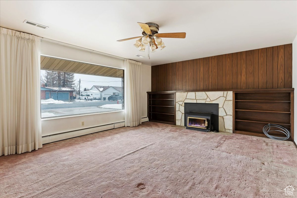 Unfurnished living room featuring baseboard heating, ceiling fan, light colored carpet, and a stone fireplace