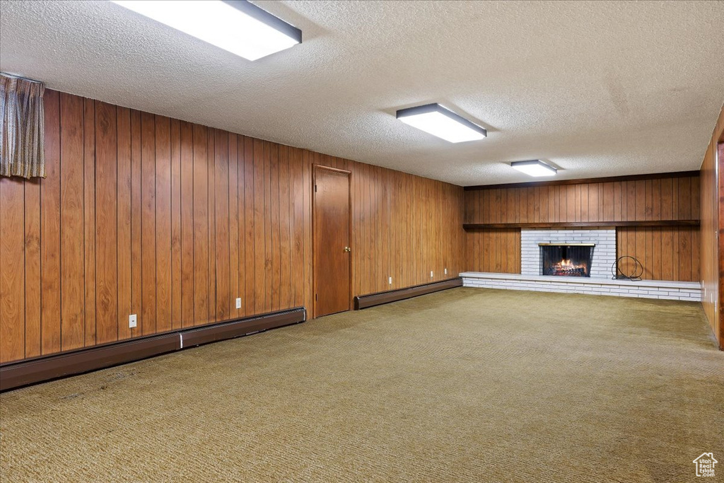 Unfurnished living room featuring a baseboard radiator, a textured ceiling, wood walls, and a brick fireplace