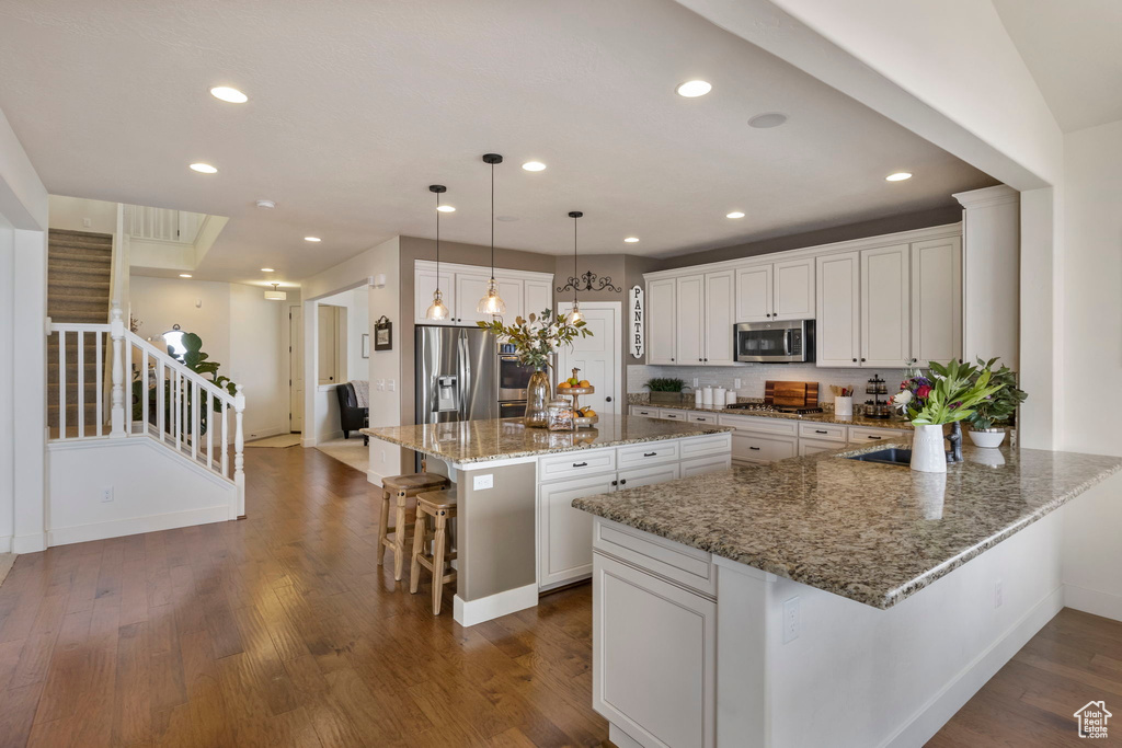 Kitchen with stainless steel appliances, white cabinets, a breakfast bar area, dark hardwood / wood-style floors, and decorative light fixtures