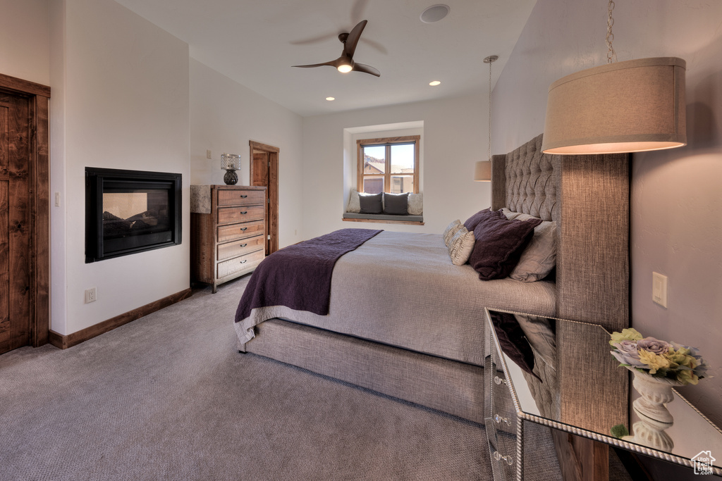 Carpeted bedroom featuring ceiling fan and a multi sided fireplace