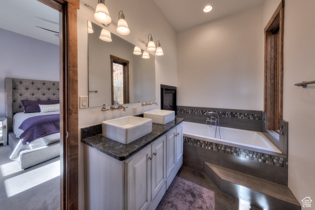 Bathroom with double sink, large vanity, an inviting chandelier, and a relaxing tiled bath