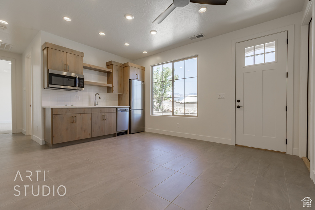 Kitchen with light tile patterned floors, sink, decorative backsplash, ceiling fan, and stainless steel appliances