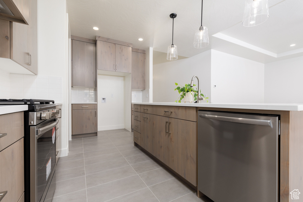 Kitchen with appliances with stainless steel finishes, light tile patterned flooring, decorative light fixtures, a tray ceiling, and tasteful backsplash