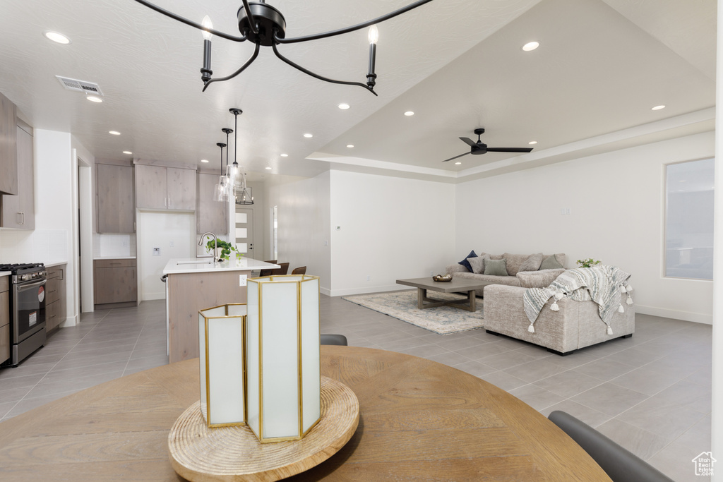 Living room with light tile patterned flooring, sink, ceiling fan with notable chandelier, and a raised ceiling