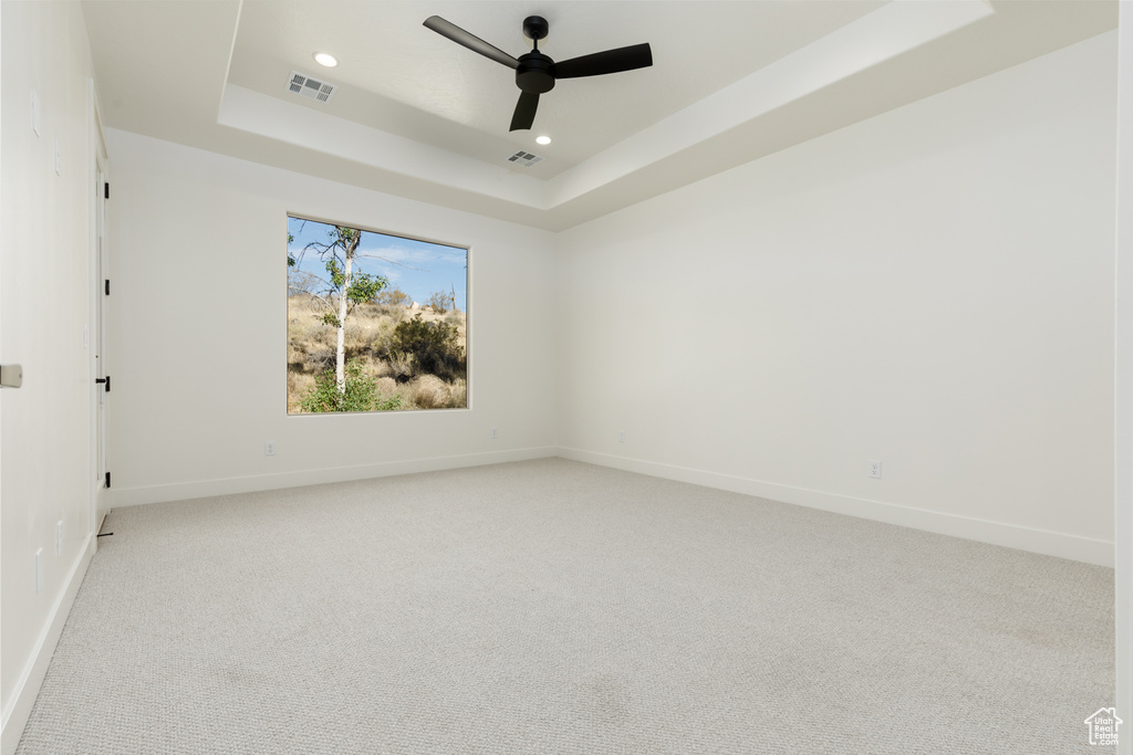 Carpeted spare room with ceiling fan and a raised ceiling