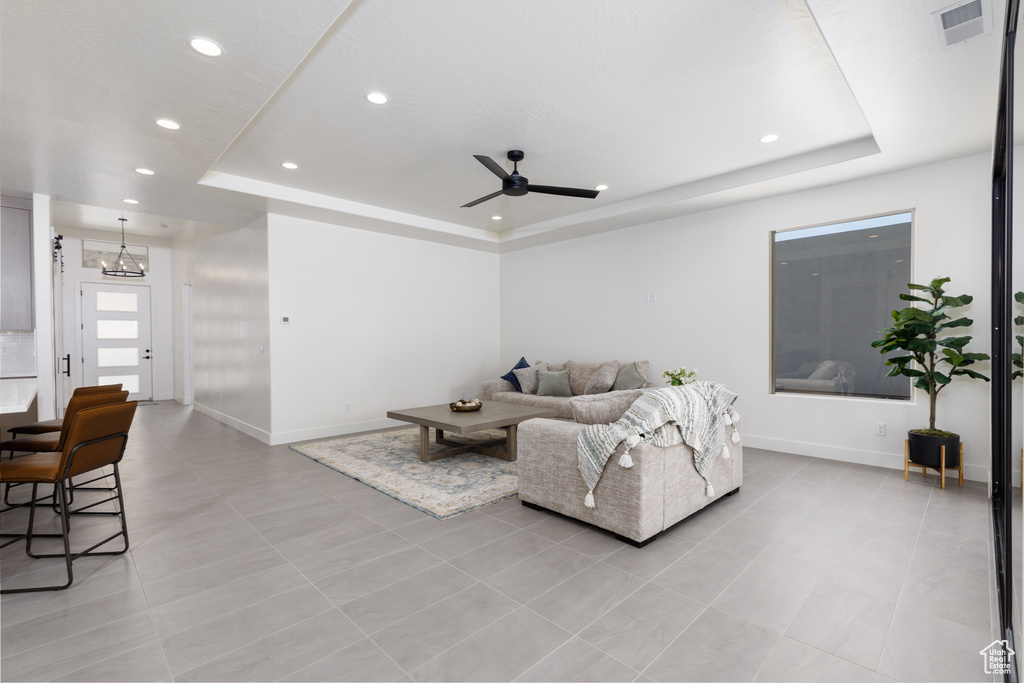 Living room featuring light tile patterned floors, ceiling fan with notable chandelier, and a tray ceiling