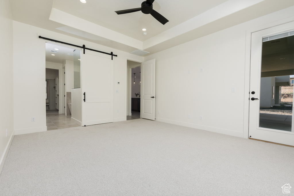 Unfurnished bedroom with ceiling fan, a barn door, light carpet, and a tray ceiling