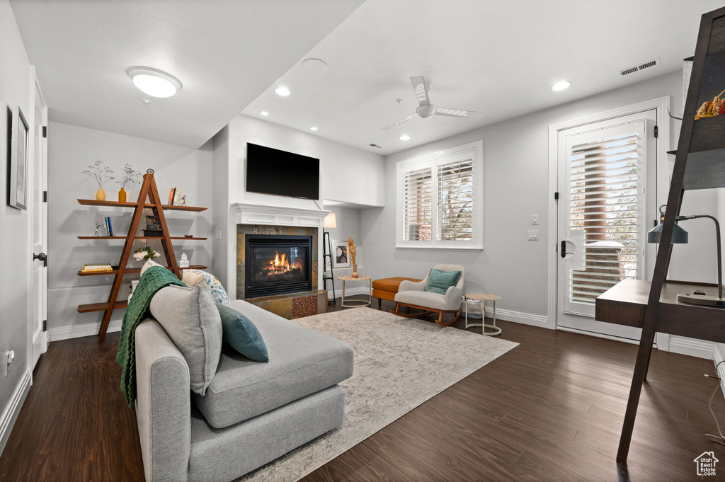 Living room with a fireplace, dark wood-type flooring, and ceiling fan