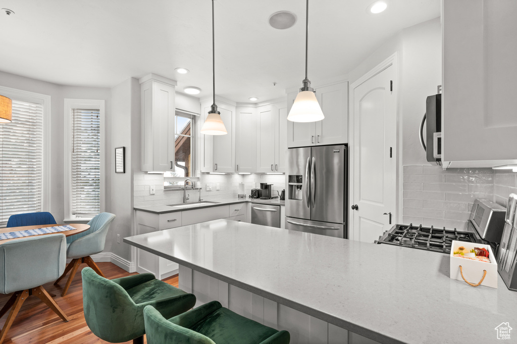 Kitchen featuring backsplash, white cabinets, sink, stainless steel appliances, and decorative light fixtures