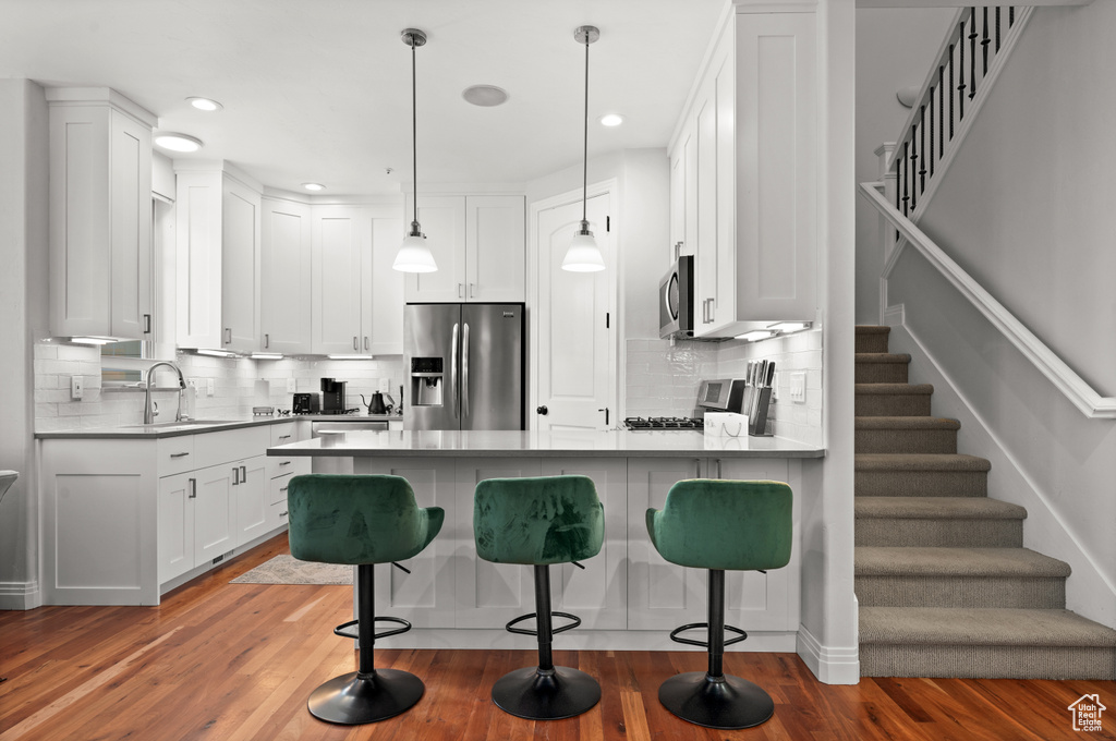 Kitchen featuring white cabinets, dark hardwood / wood-style flooring, hanging light fixtures, and appliances with stainless steel finishes