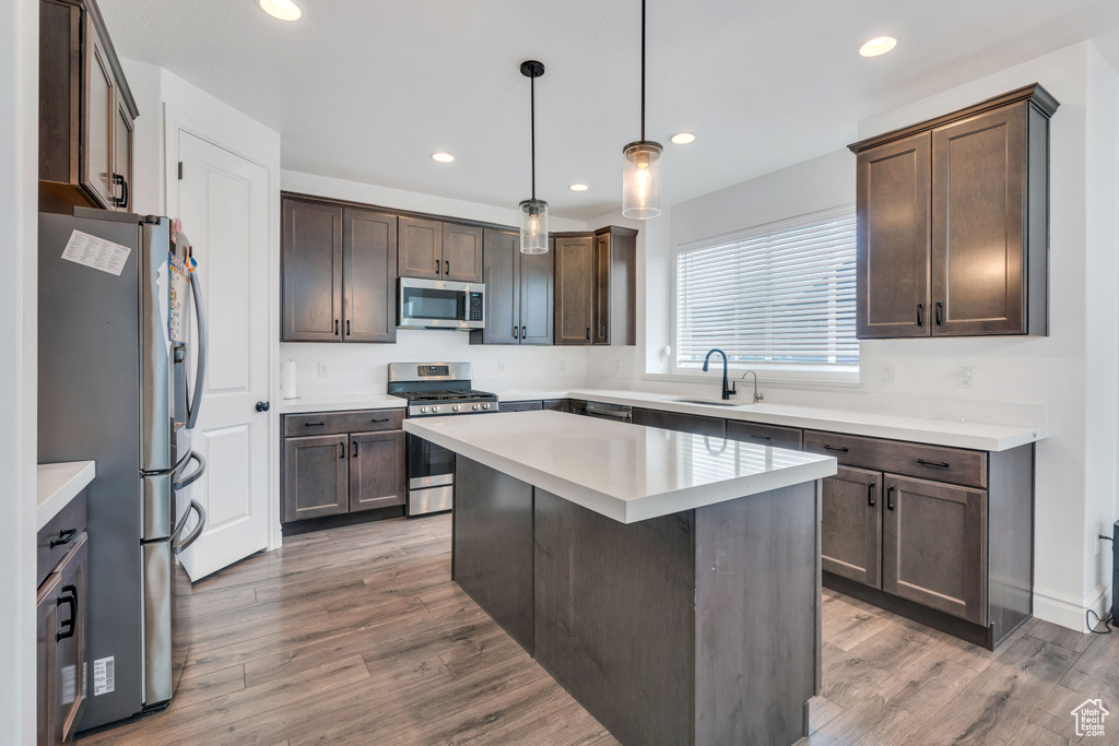 Kitchen featuring a kitchen island, sink, hardwood / wood-style flooring, pendant lighting, and appliances with stainless steel finishes