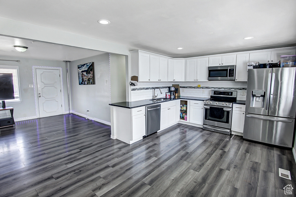 Kitchen with backsplash, white cabinets, dark wood-type flooring, sink, and appliances with stainless steel finishes