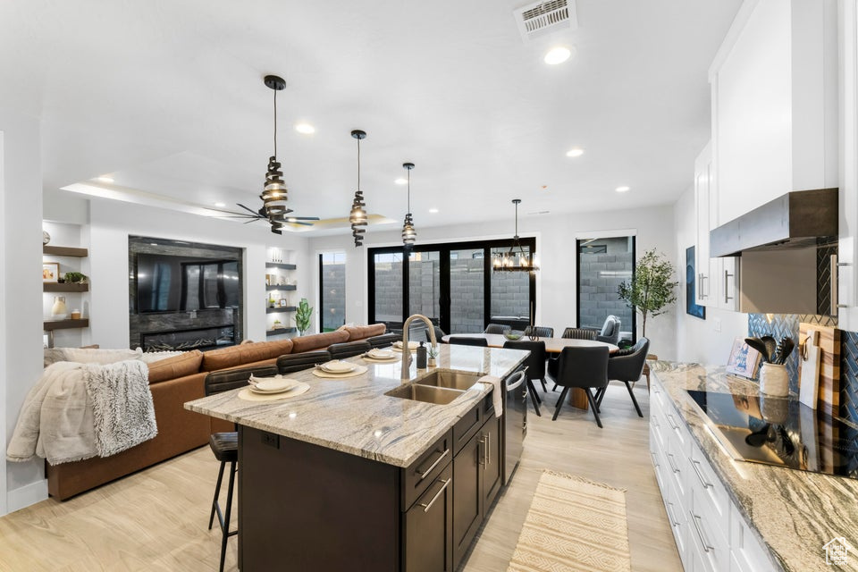 Kitchen with a kitchen island with sink, white cabinets, a breakfast bar area, hanging light fixtures, and ceiling fan with notable chandelier