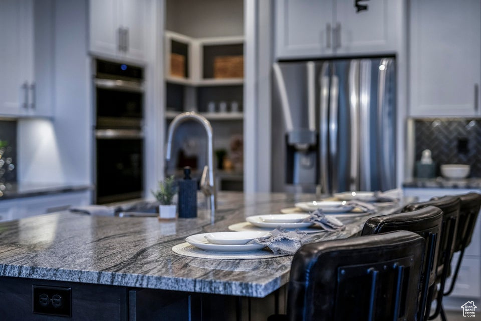 Kitchen featuring white cabinetry, a kitchen island with sink, stainless steel appliances, and backsplash