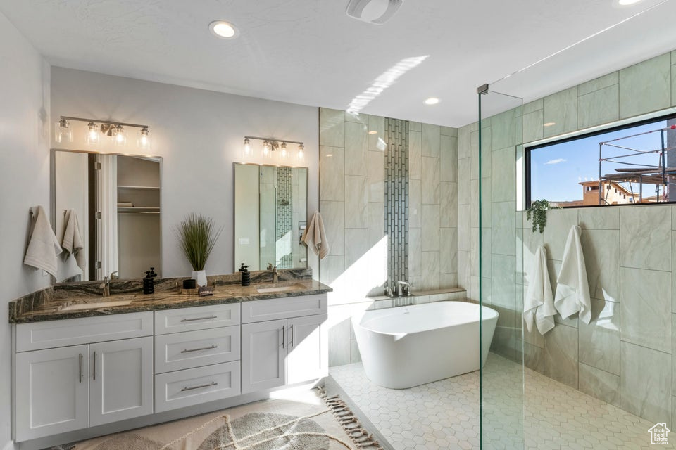 Bathroom with dual sinks, tile flooring, separate shower and tub, and vanity with extensive cabinet space