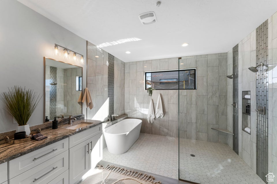 Bathroom featuring plus walk in shower, dual bowl vanity, tile walls, and tile floors