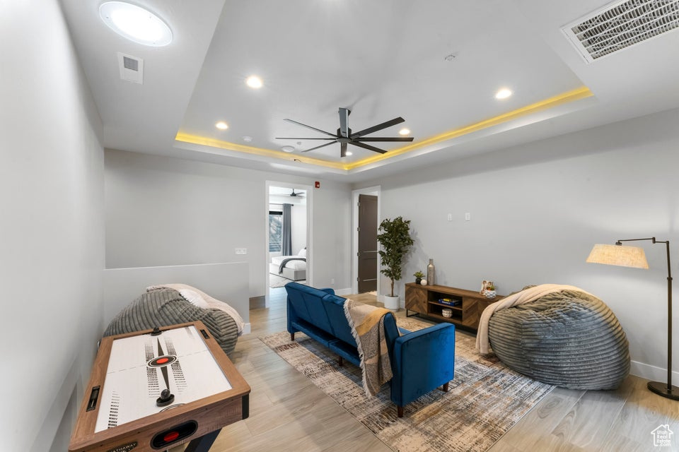 Living room with light hardwood / wood-style floors, ceiling fan, and a raised ceiling