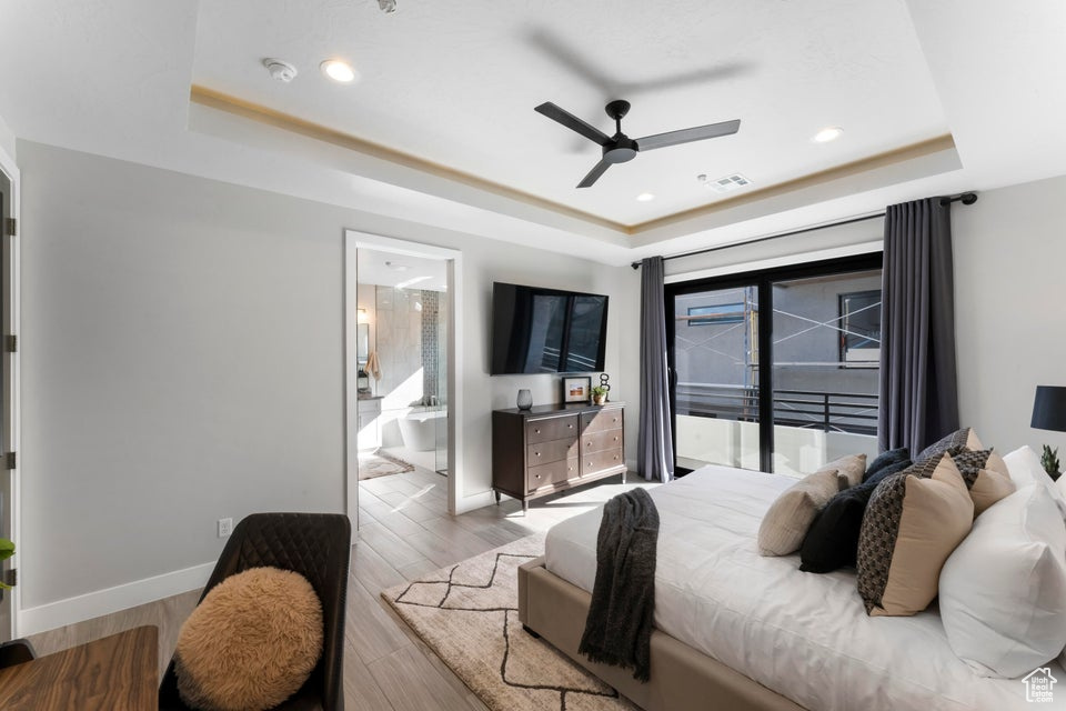Bedroom with light wood-type flooring, access to exterior, a tray ceiling, and ceiling fan