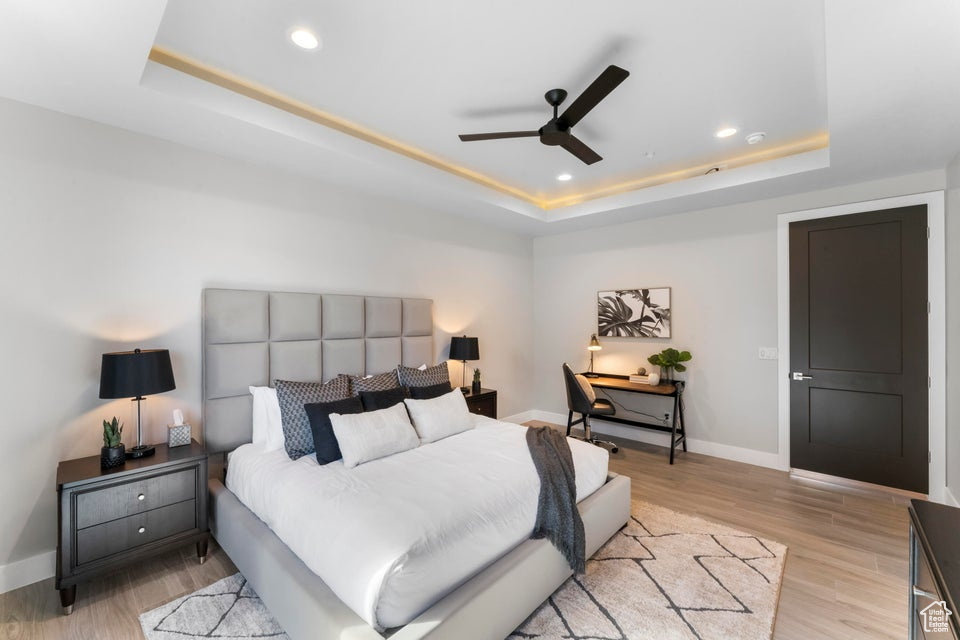 Bedroom with light hardwood / wood-style flooring, ceiling fan, and a raised ceiling