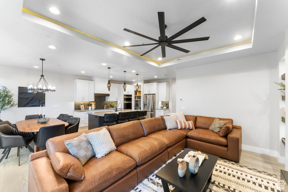 Living room with light hardwood / wood-style flooring, a tray ceiling, ceiling fan with notable chandelier, and sink