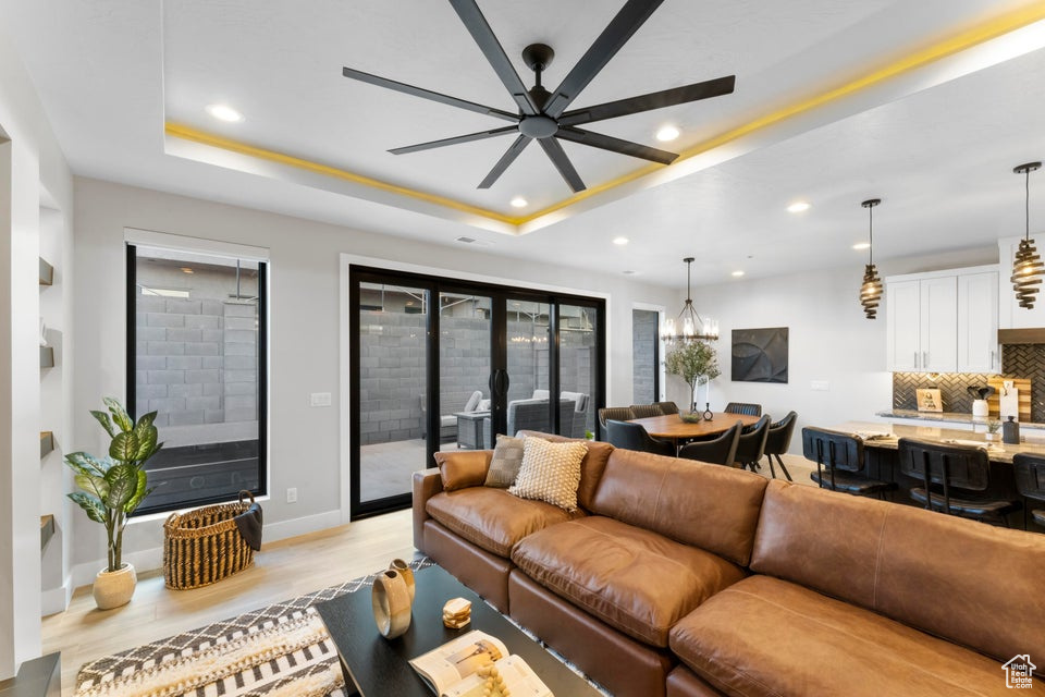 Living room with ceiling fan with notable chandelier, a raised ceiling, and light hardwood / wood-style flooring