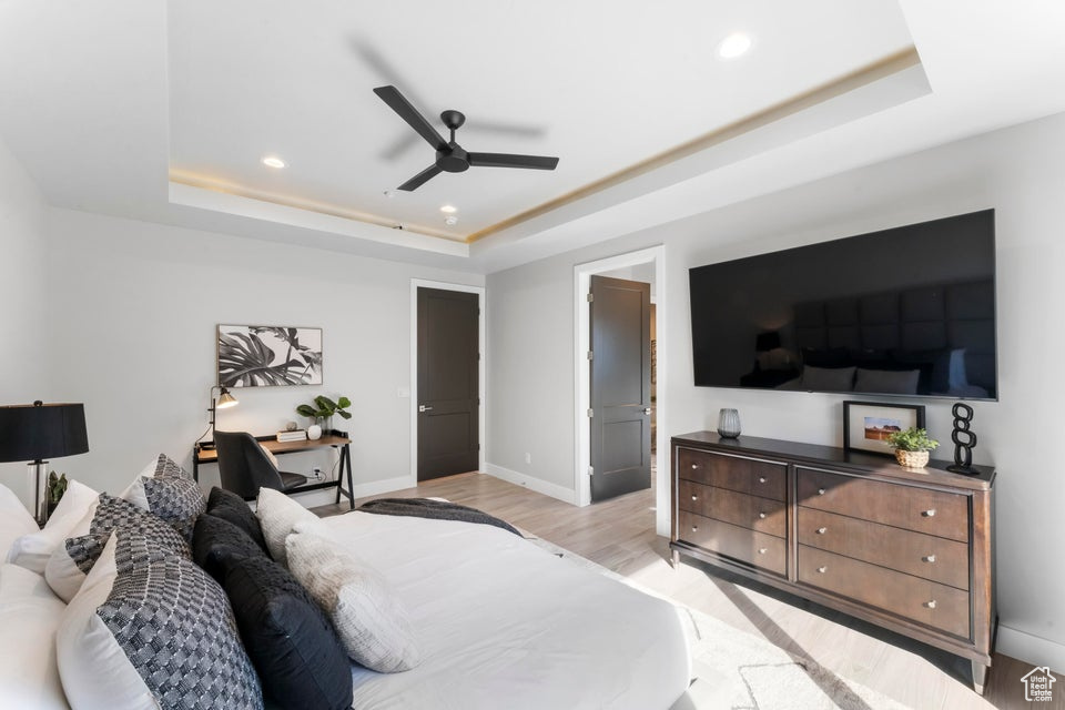 Bedroom featuring light hardwood / wood-style flooring, a raised ceiling, ensuite bathroom, and ceiling fan