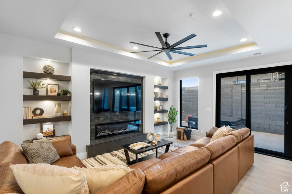 Living room featuring light hardwood / wood-style floors, a raised ceiling, ceiling fan, built in features, and a tile fireplace