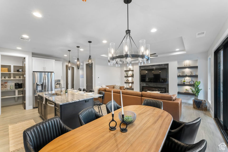 Dining area featuring light hardwood / wood-style flooring, an inviting chandelier, sink, built in features, and a tray ceiling