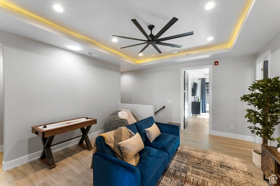Interior space with ceiling fan, a tray ceiling, and light wood-type flooring