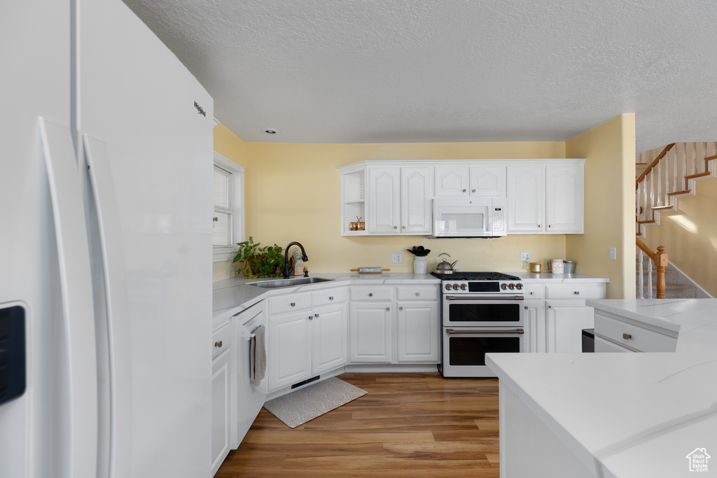 Kitchen featuring light wood-type flooring, white cabinets, a textured ceiling, sink, and double oven range