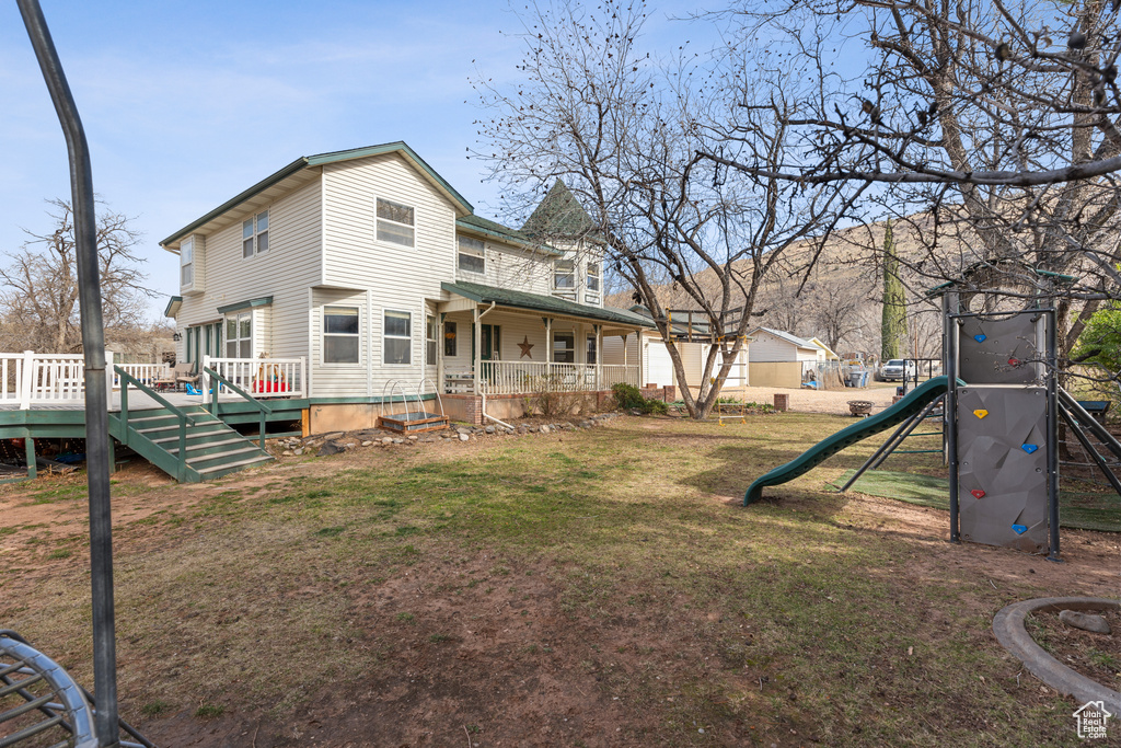 Back of house featuring a wooden deck, a lawn, and a playground