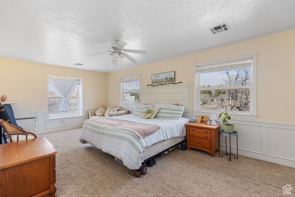Bedroom featuring ceiling fan, light colored carpet, multiple windows, and a textured ceiling