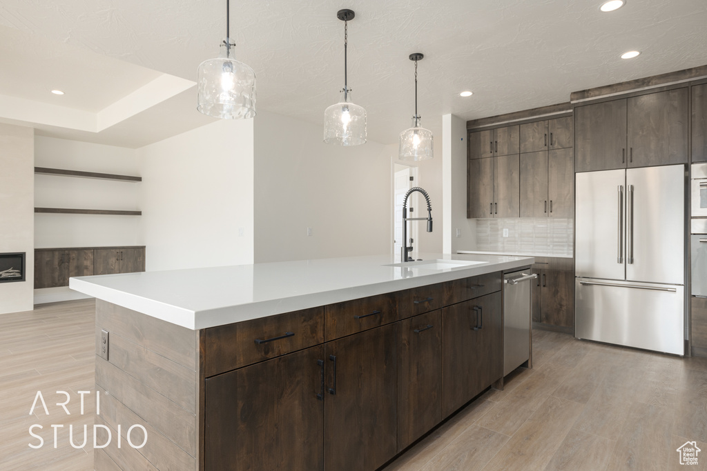 Kitchen with pendant lighting, a center island with sink, appliances with stainless steel finishes, light wood-type flooring, and sink