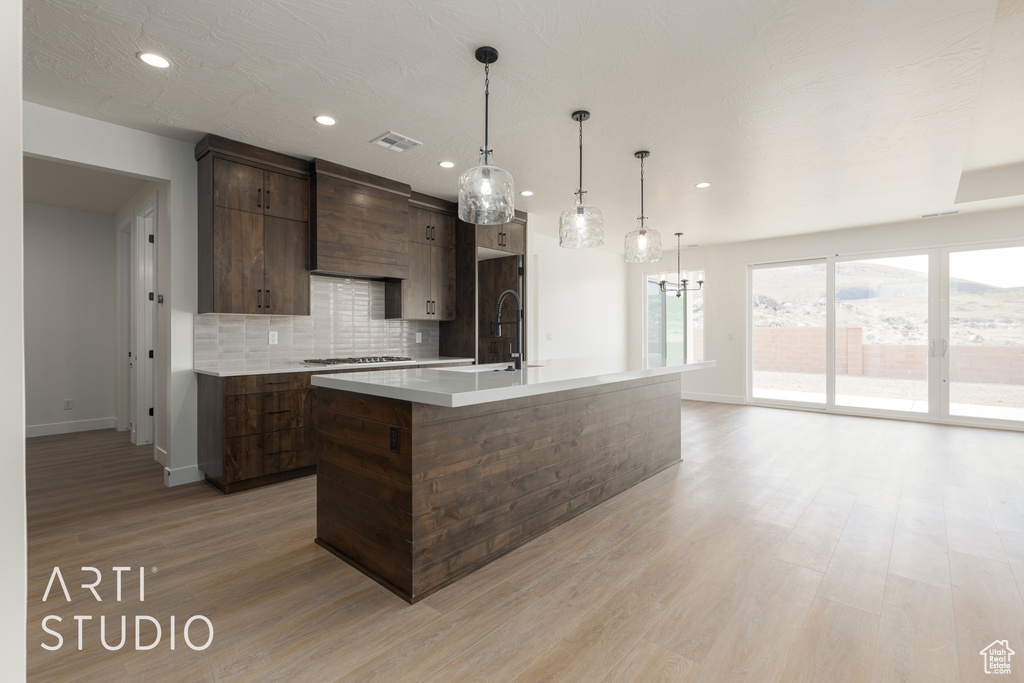 Kitchen with a kitchen island with sink, pendant lighting, light hardwood / wood-style flooring, backsplash, and premium range hood